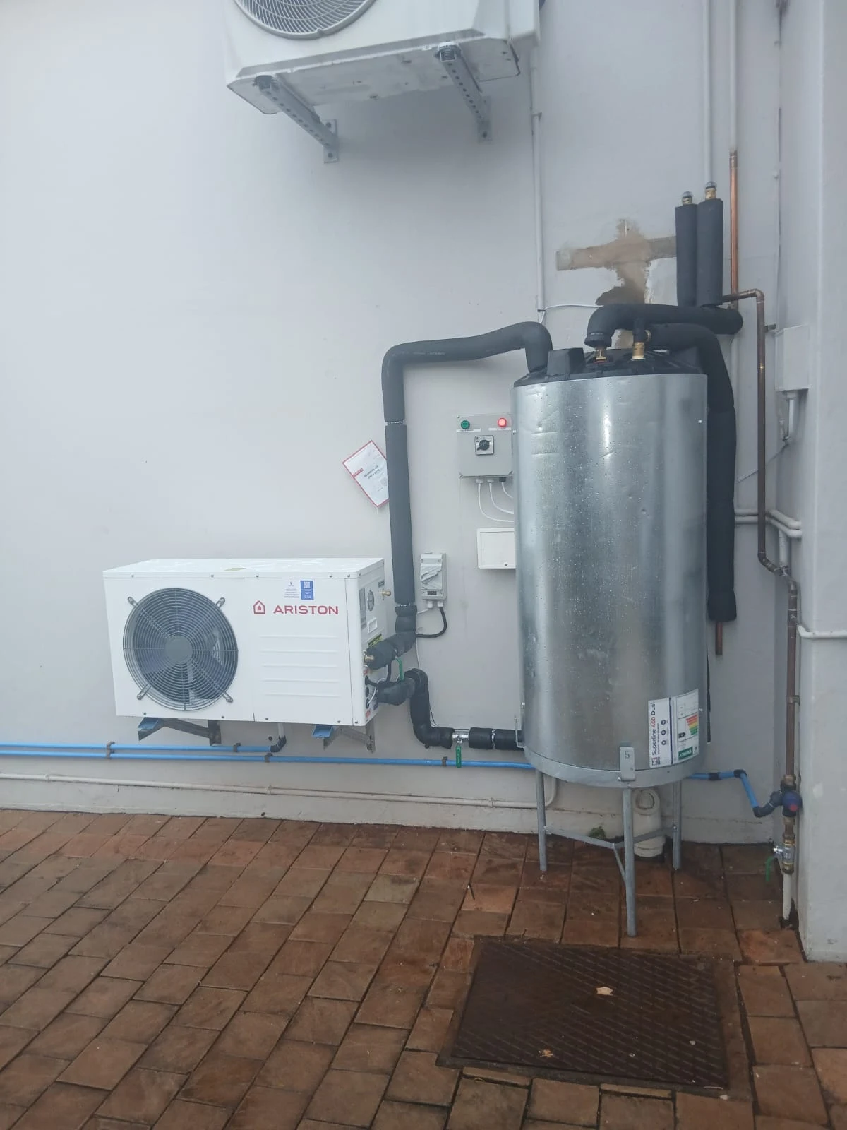 A pressure vessel and pump installed against an outside wall above brick paving