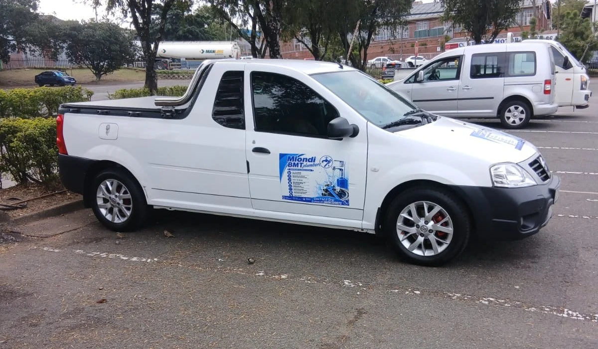 A white bakkie parked on tarmac with Mlondi BMT Plumbers signage on the driver's door