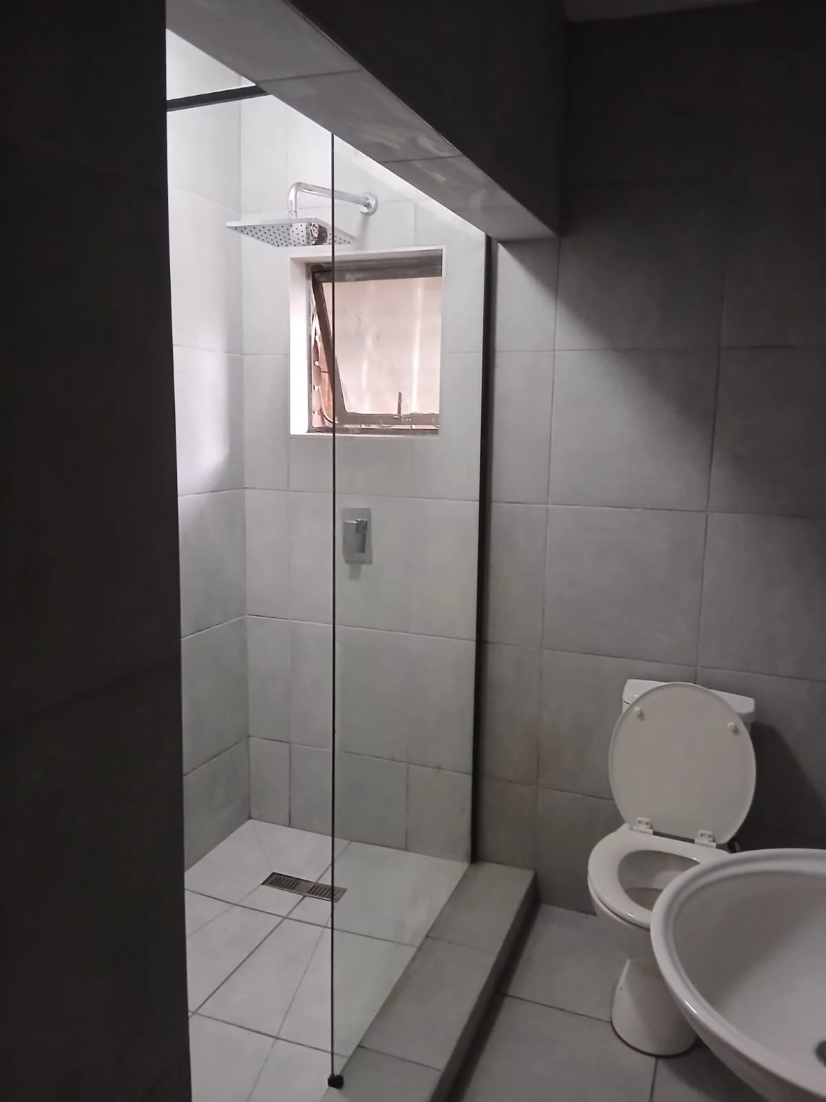 A finished shower cubicle tiled in large grey tiles, with a glass screen, rain shower head, recessed mixer and a linear drain in the floor