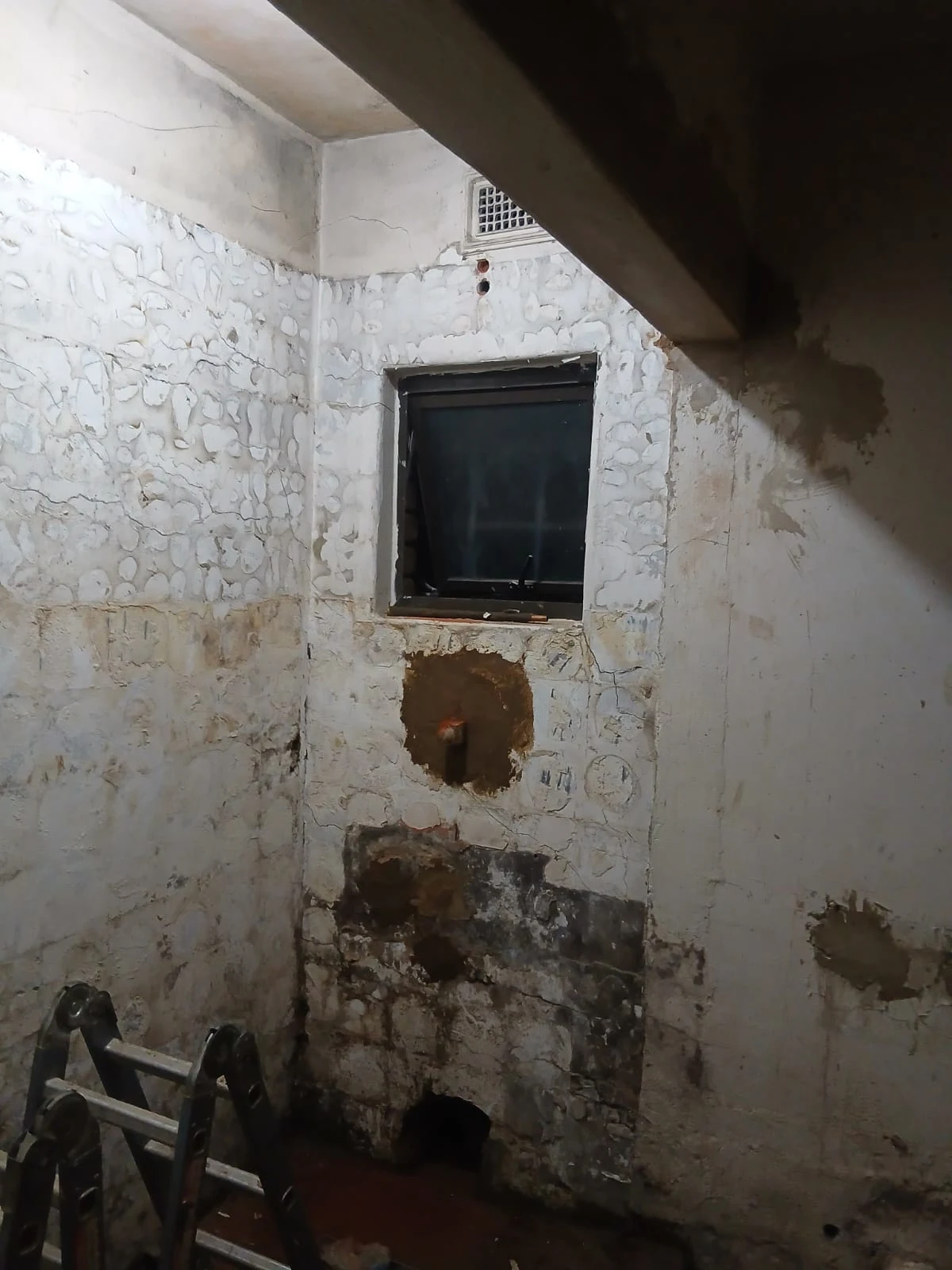 A bathroom stripped back to bare brick and concrete, with old pipework chased out of the wall and a ladder standing in the corner