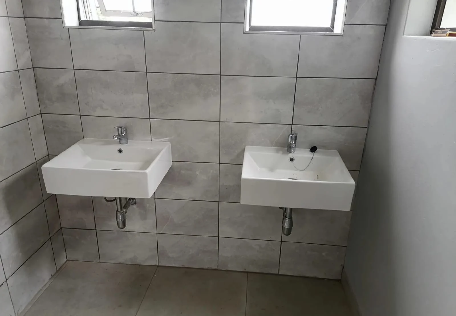 Two square wall-hung basins side by side on a tiled wall
